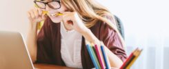 woman biting pencil while sitting on chair in front of computer during daytime